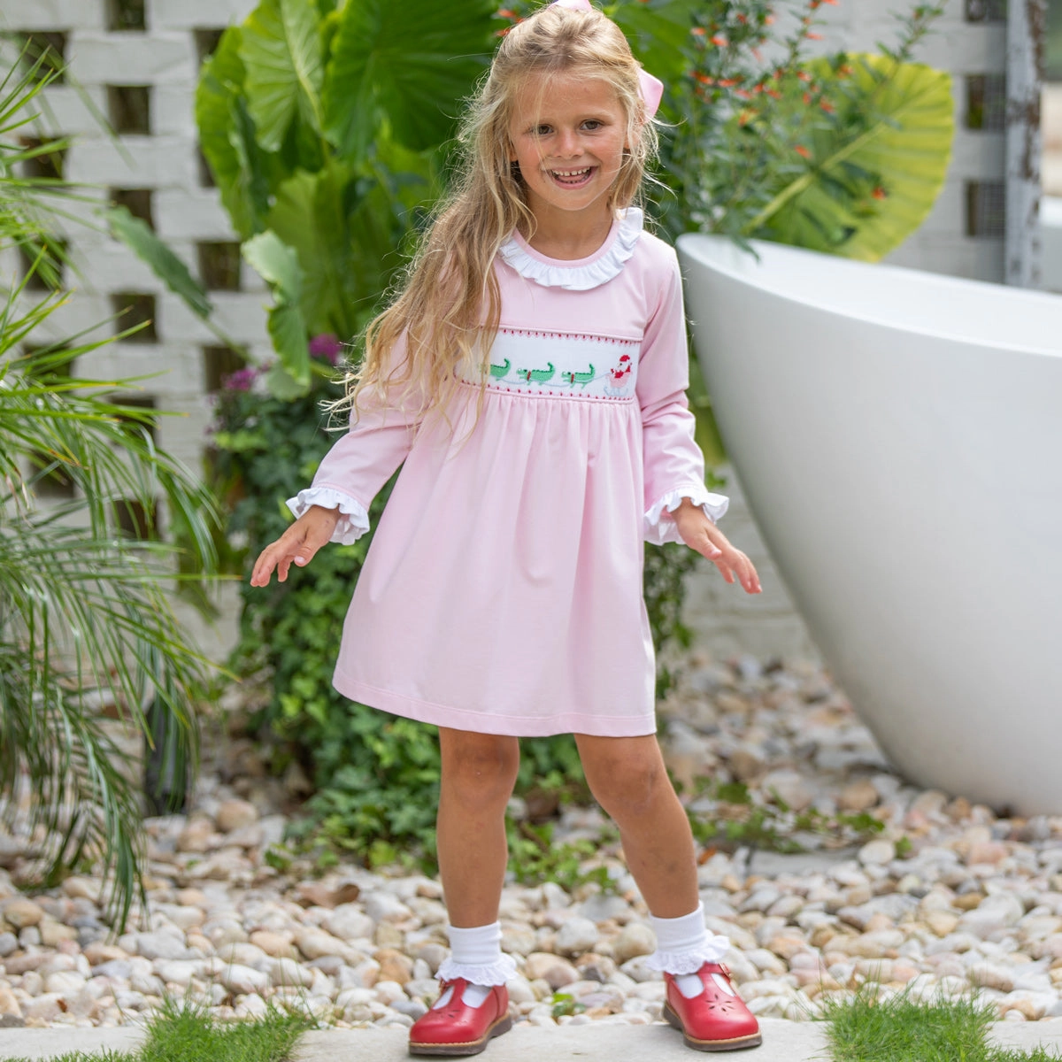 Girl in a pink smocked dress with a bow in a garden