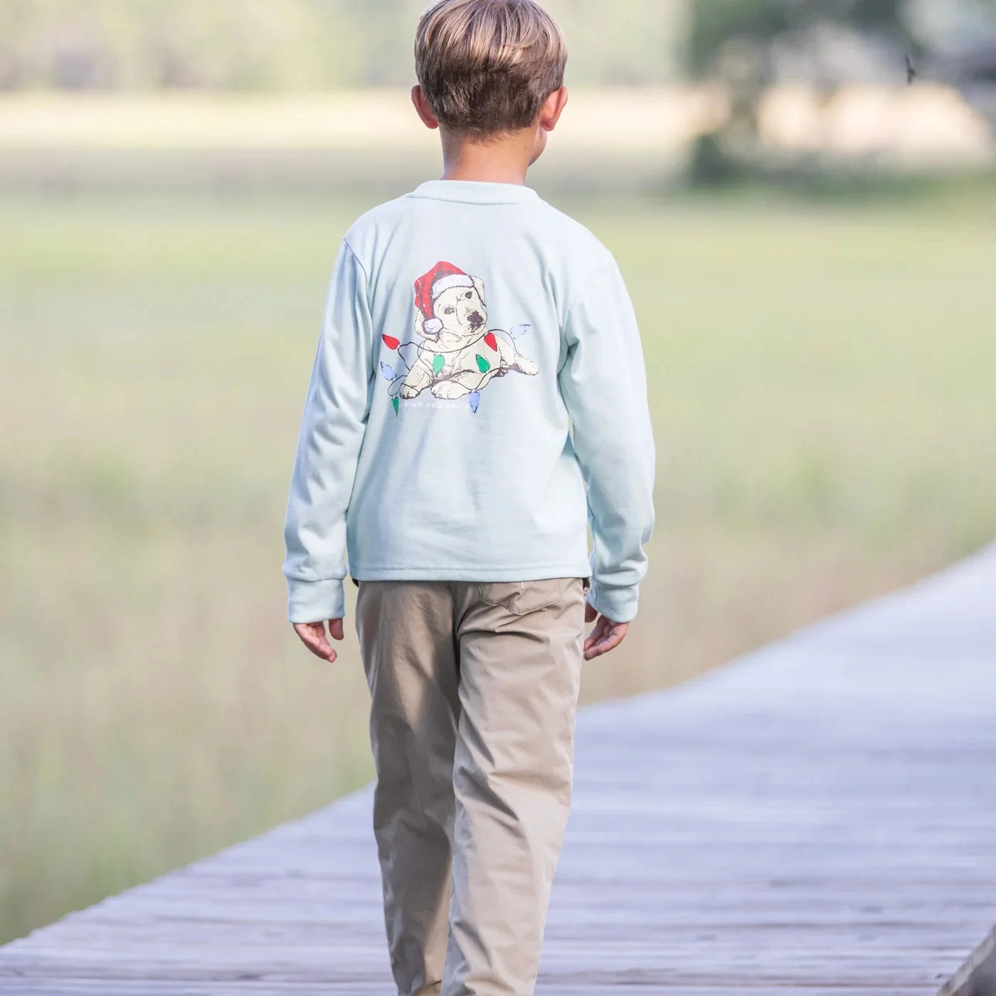 Boy seen from behind in a graphic tee and khakis on a boardwalk