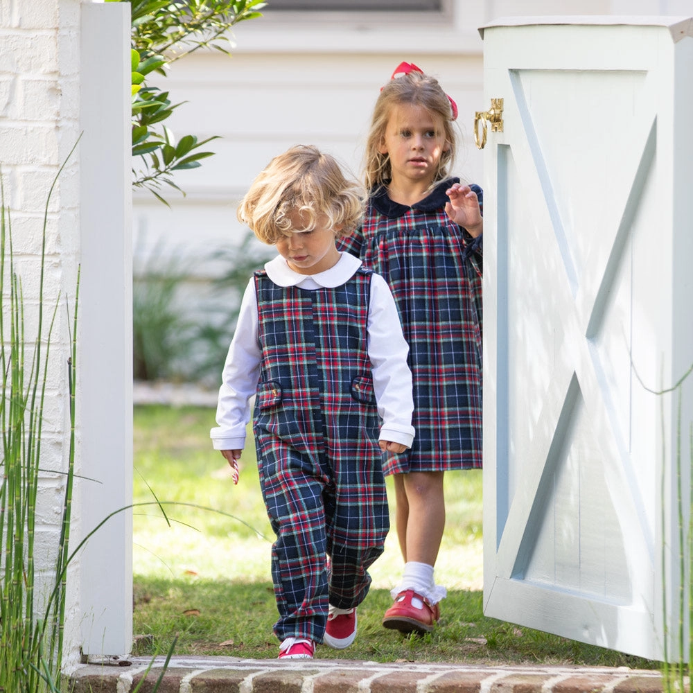 Boy and girl in matching navy tartan outfits walking through a white barn door